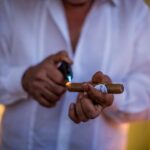 Man in white shirt lighting a cigar with a torch lighter, cigar band visible, warm ambient lighting